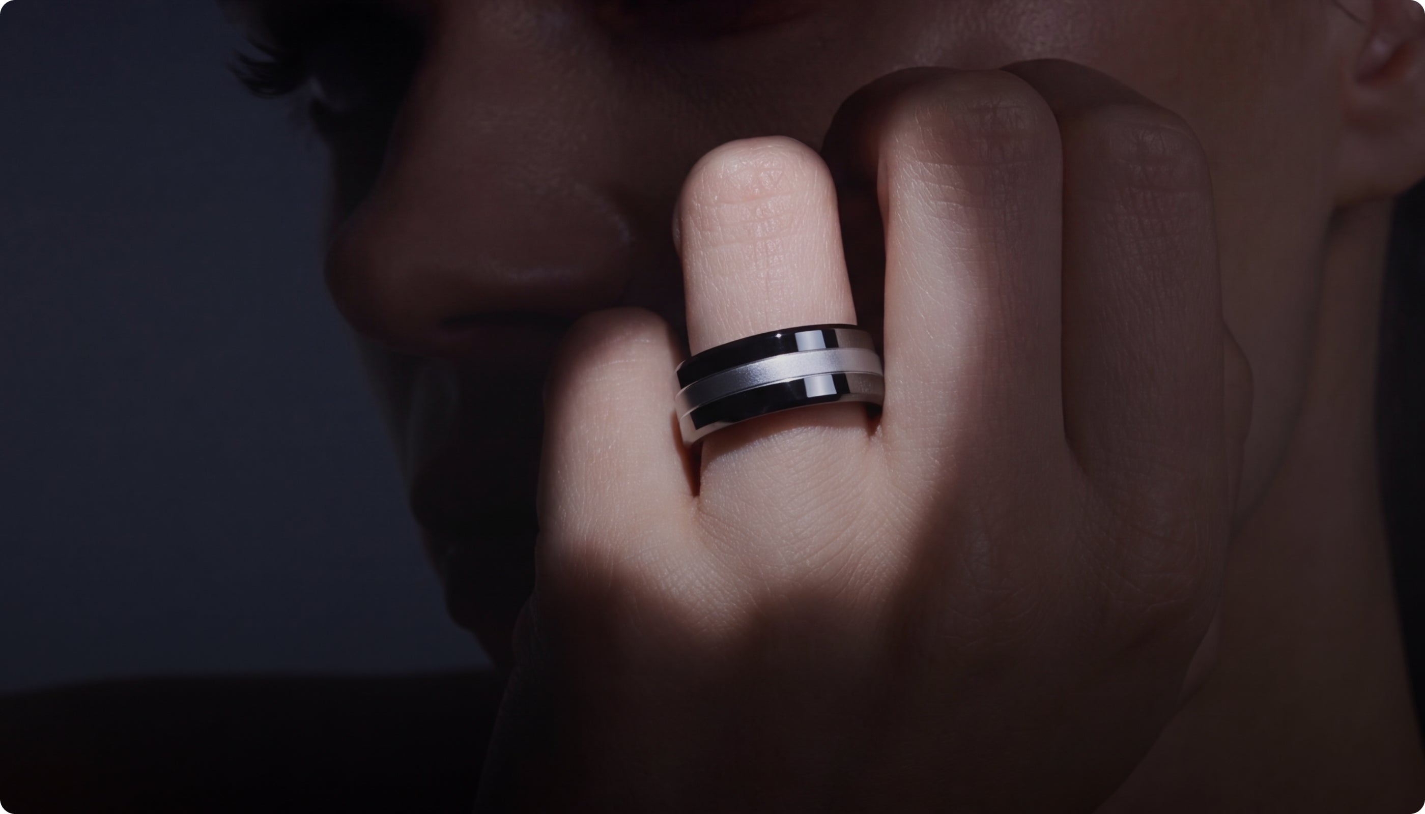 A close-up lifestyle shot of a person wearing a Signal Ring with a black inlay on their ring finger, set against a dark, moody background.